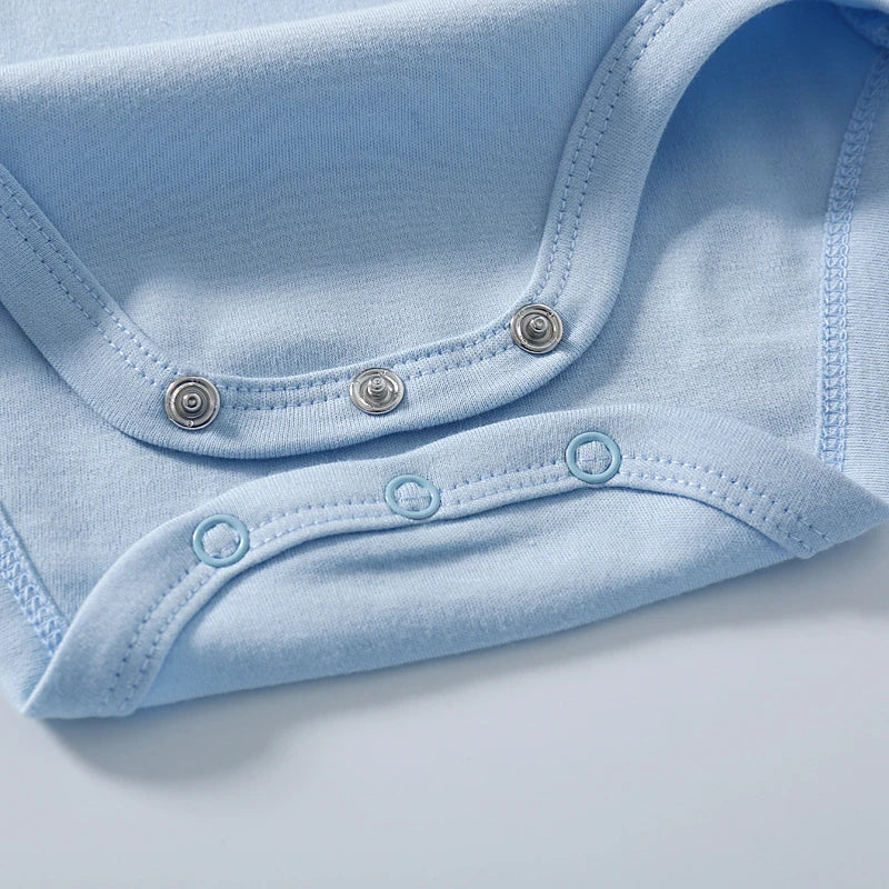Gros plan d'un Body Coton Imprimé bleu clair de BABY-PREMA posé à plat. L'image met en valeur les boutons pression situés en bas du vêtement. Le tissu semble doux et confortable, avec des bords soigneusement finis, parfait pour les journées chaudes.