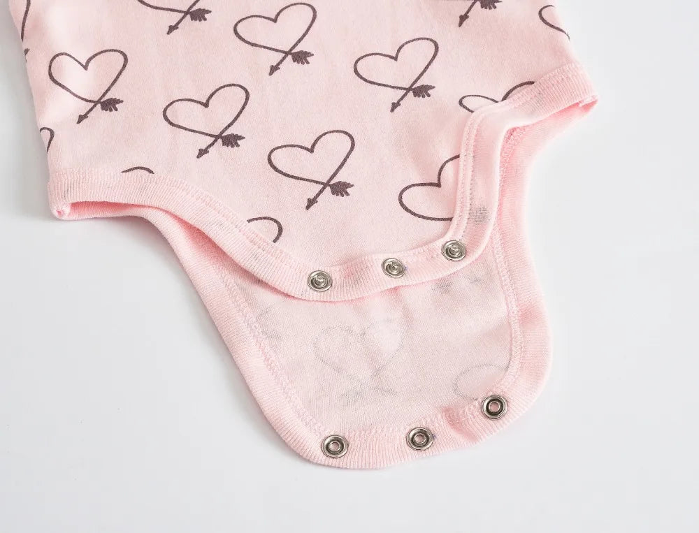 Gros plan sur un Lot de 7 Bodies Bébé Imprimés Unis de BABY-PREMA en coton doux avec imprimé coeur et flèche, comportant des boutons pression en bas.