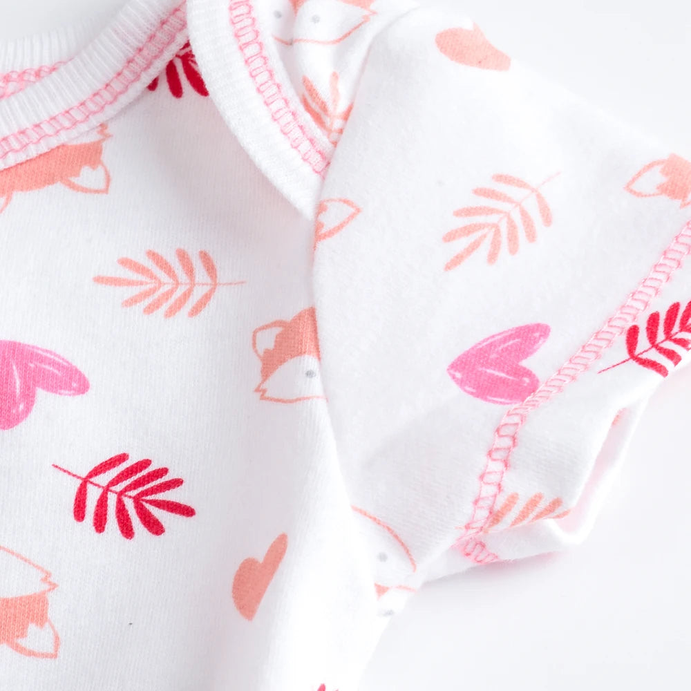 Un gros plan d'un Lot de 7 Bodies Bébé Imprimés Unis en coton blanc par BABY-PREMA avec des motifs roses et rouges de cœur, de feuille et de renard avec des coutures roses le long des bords et des boutons pression pratiques pour un change facile.