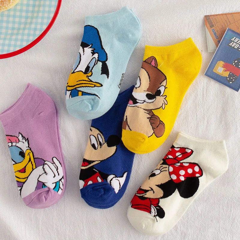 Une collection de cinq Paires Chaussettes Coton Coréennes colorées de BABY PREMA mettant en vedette divers personnages Disney. Les chaussettes représentent Donald Duck, Daisy Duck, Mickey Mouse, Minnie Mouse et Chip. Fabriqués en coton léger et confortable, ils sont disposés sur une surface blanche aux côtés d'une assiette de dessert et d'un livre.