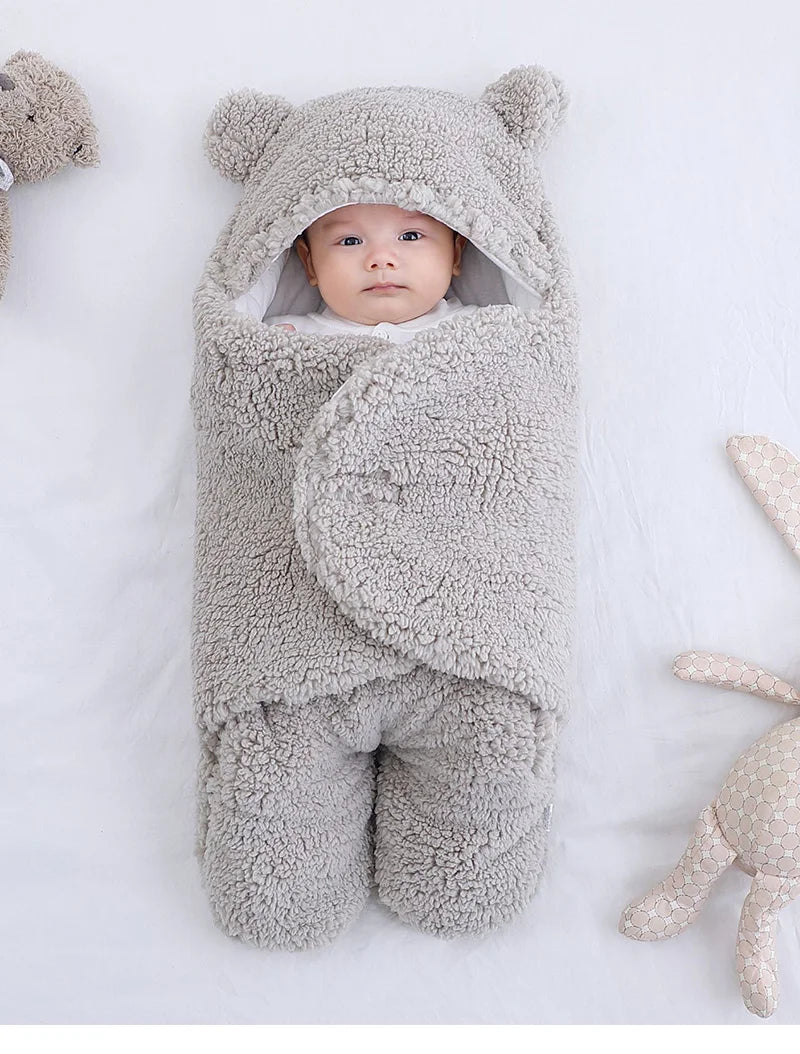 Un bébé douillet enveloppé dans une gigoteuse BABY-PREMA Couverture Doux Bébé 0-9 mois, qui regarde avec des yeux curieux, entouré d'accessoires bébé.