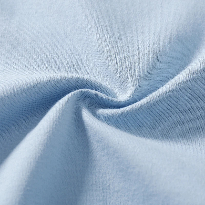 Gros plan d'un tissu bleu clair à la texture douce, mettant en valeur un subtil pli torsadé au milieu. Le matériau semble lisse et confortable, parfait pour un Body Coton Imprimé BABY-PREMA, donnant une sensation de drapé doux et de flexibilité idéale pour les journées chaudes.