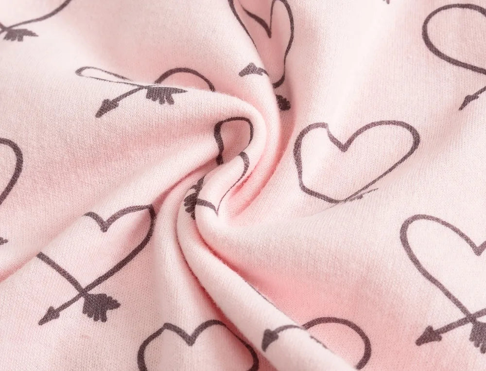 Gros plan sur un tissu en coton rose avec un motif de coeurs et de flèches noirs. Le centre légèrement froissé laisse penser qu'il pourrait s'agir d'un de ces Lot de 7 Bodies Bébé Imprimés Unis de BABY-PREMA, parfaits pour les peaux délicates.