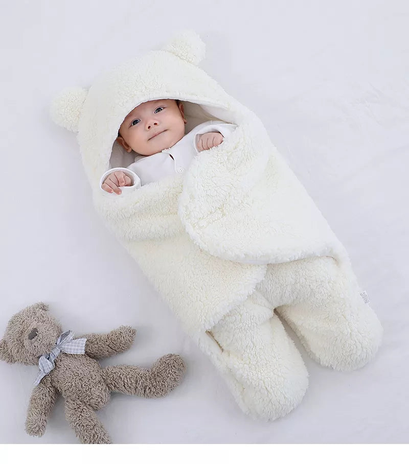 Un bébé joyeux bien enveloppé dans une Couverture Doux Bébé 0-9 mois de BABY-PREMA, avec un ours en peluche à ses côtés, entouré de charmants accessoires bébé.