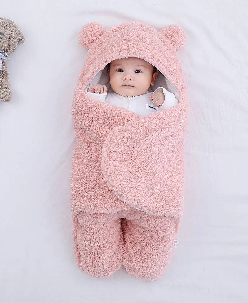 Un bébé douillet enveloppé dans une Couverture Doux Bébé 0-9 mois de BABY-PREMA, avec de petites oreilles, allongé à côté d'un ours en peluche et d'un article bébé, regardant calmement la caméra.