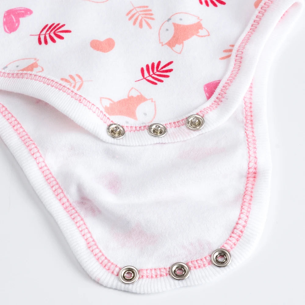 Gros plan d'une combinaison blanche pour bébé avec des coutures roses et des imprimés renard et cœur. Cette pièce douillette du Lot de 7 Bodies Bébé Imprimés Unis, en coton doux, comporte des boutons-pression en métal pour la fermeture BABY-PREMA.