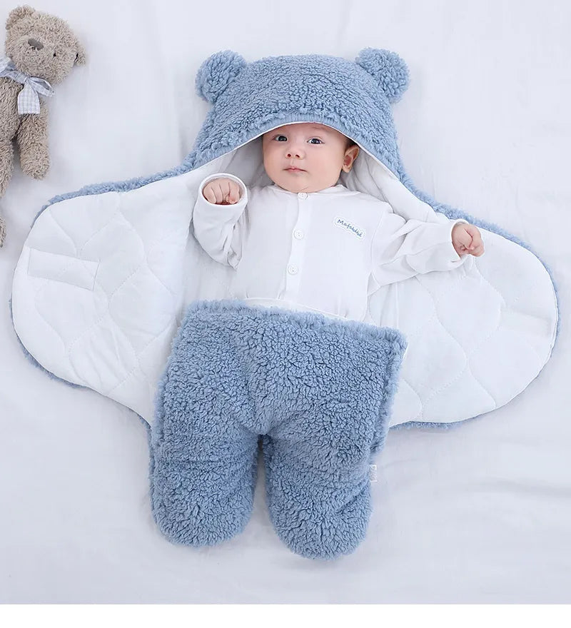 Un bébé douillet blotti dans une couverture BABY-PREMA Doux Bébé 0-9 mois, dotée d'une jolie capuche ornée d'oreilles et d'une texture douce et pelucheuse, regarde calmement l'appareil photo, avec accès à un ours en peluche.