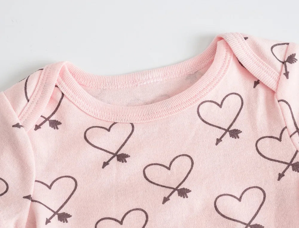 Vue rapprochée d'une combinaison bébé rose en coton doux doux. Le Lot de 7 Bodies Bébé Imprimés Unis de BABY-PREMA, parfait pour les nouveaux parents, présente un motif de contours de cœurs noirs traversés par des flèches.