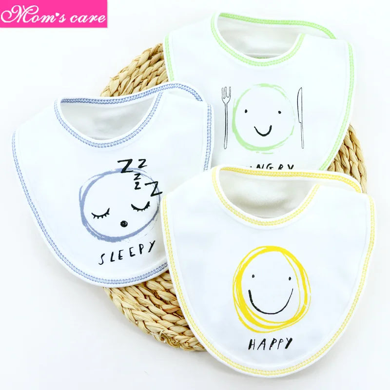 Trois Lot de 3 pièces Bavoirs Bébé aux motifs de smileys, en coton de haute qualité, sont disposés sur un couvercle de panier en osier. Les bavoirs bébé BABY-PREMA affichent différentes ambiances : un visage endormi avec le texte « SLEEPY », un visage joyeux avec le texte « HAPPY » et un visage avec des ustensiles symbolisant « HUNGRY ». Une étiquette « Soins de maman » se trouve en haut à gauche.