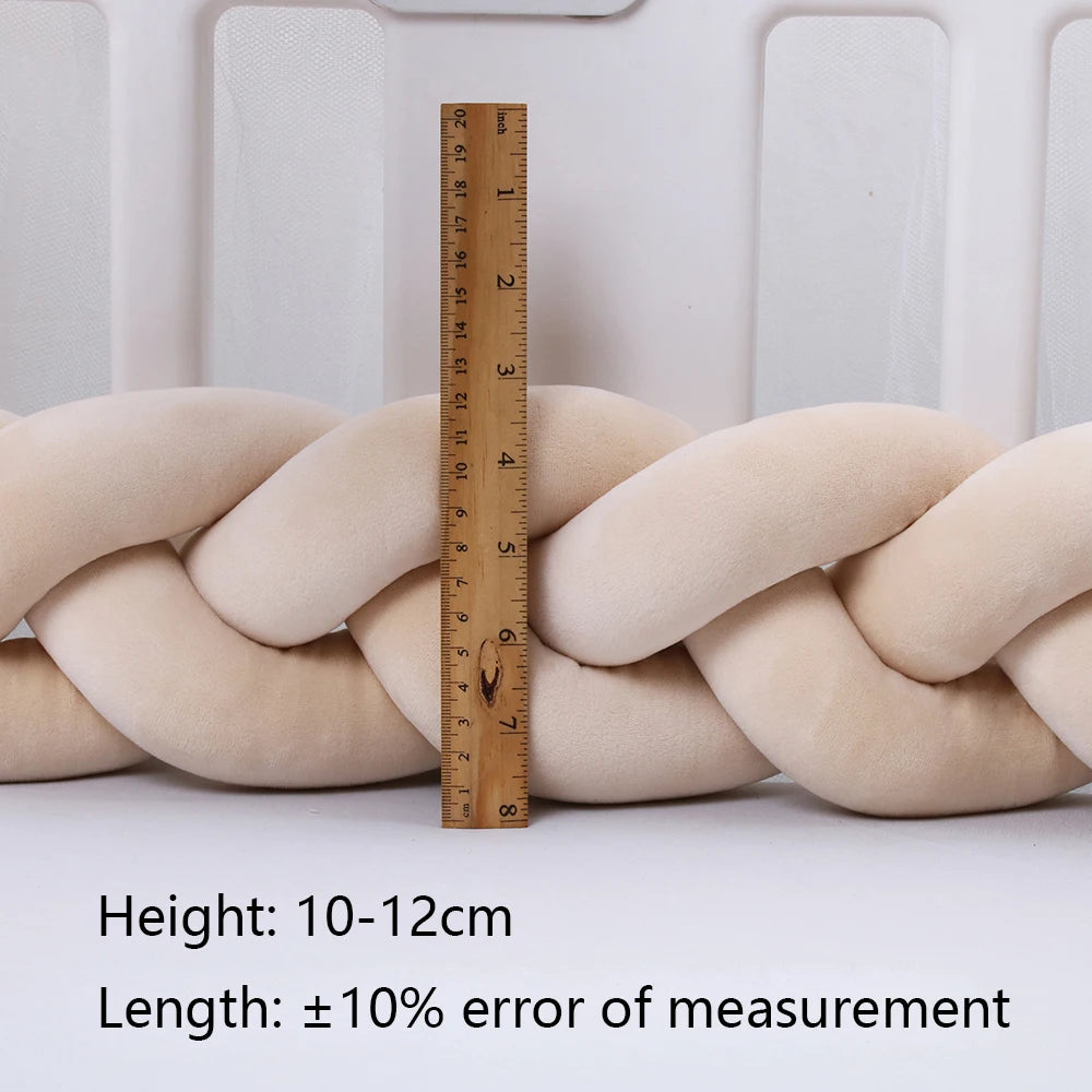 Un BABY PREMA Tour de lit Bébé Tressé Noué est posé verticalement contre un grand coussin tressé beige pour montrer sa hauteur. La hauteur du coussin varie de 10 à 12 cm selon le texte superposé, qui note également une erreur de mesure de longueur de plus ou moins 10 %. Idéal comme tour de lit pour bébé pour assurer la sécurité de votre bébé.