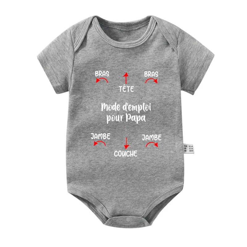 Une combinaison bébé grise à manches courtes - "Body Coton Imprimé" par BABY-PREMA - avec un texte français et des flèches rouges pointant vers différentes parties. Le texte dit "Mode d'emploi pour Papa" avec des flèches intitulées "Bras" pour les bras, "Tête" pour la tête, "Jambe" pour les jambes et "Couche" pour la couche. Parfait pour un nouveau-né !