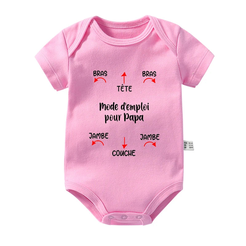 Un Body Coton Imprimé rose de BABY-PREMA est présenté avec un texte en français qui se traduit par « Instructions pour papa », parfait pour les journées chaudes. Il y a des flèches directionnelles intitulées « soutiens-gorge » (bras), « tête » (tête), « jambe » (jambe) et « canapé » (couche) pointant vers différentes parties de la barboteuse en coton.