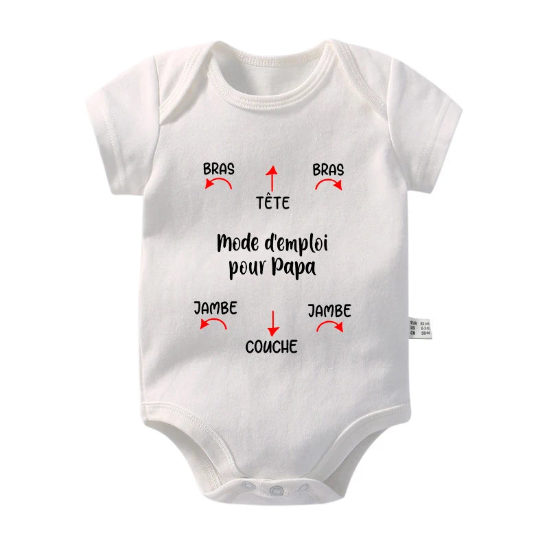 Une combinaison pour bébé en coton blanc avec un texte français noir indiquant « Mode d'emploi pour Papa », avec des flèches pointant vers des parties étiquetées comme « BRAS » (bras) et « TÊTE » (tête). Cet adorable Body Coton Imprimé de BABY-PREMA assure que votre bébé reste confortable pendant les journées chaudes tout en étant facile à habiller.