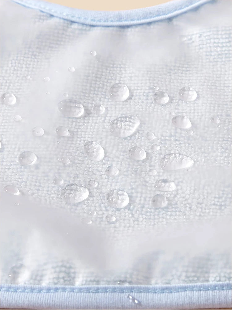Une image en gros plan de gouttelettes d'eau sur une surface en tissu texturé bleu clair avec un design bandana unique. Le tissu semble très résistant à l’eau, car les gouttelettes perdent plutôt que de pénétrer dans le matériau. Les bords des Bavoirs Bébé Lot de 4 Pièces de BABY-PREMA sont visibles en haut et en bas de l'image.