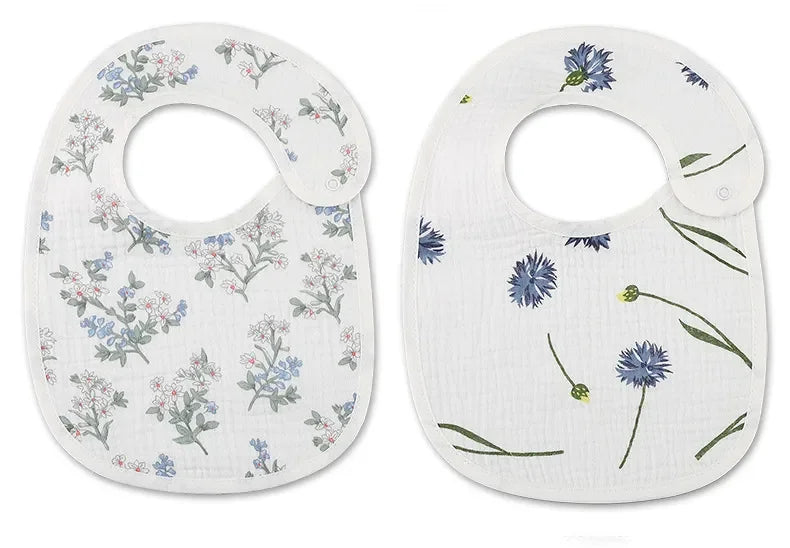 Deux BABY-PREMA Bavoirs Motifs Bébé 2 Pièces blancs à motifs floraux. L'un a des fleurs roses et bleues ; l'autre a des fleurs bleues avec des tiges vertes. Chaque bavoir comporte une fermeture à un seul bouton.