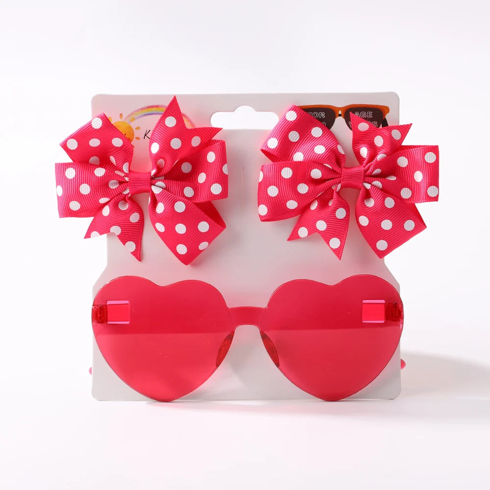Un paquet contenant deux bandeaux à nœuds en nylon à pois rouges et une paire de lunettes de soleil pour bébé en forme de coeur rouge sur fond blanc de l'Ensemble d'Accessoires Bébé | Lunettes de Cheveux pour Bébé de BABY PREMA.