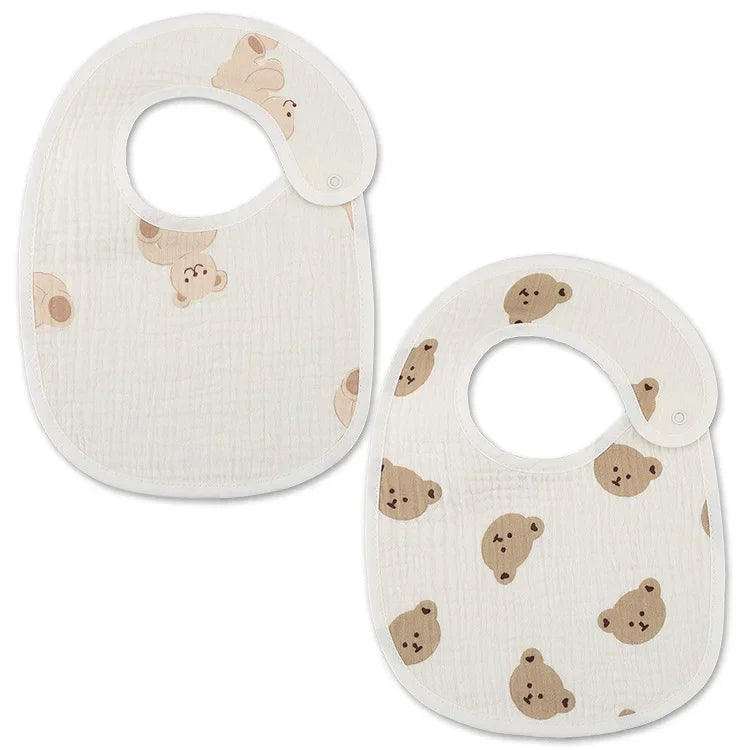 Deux bavoirs blancs avec de jolis visages d'ours marron imprimés dessus. Ces Bavoirs Motifs Bébé 2 Pièces de BABY-PREMA comportent des fermetures à pression au niveau du cou et sont fabriqués dans un tissu doux et texturé, conçu dans un charmant style Bandana.