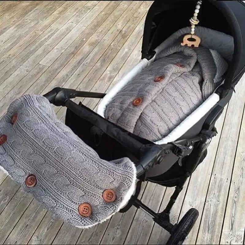 Une poussette double Baby Prema douillette avec des chancelières grises en tricot doux ornées de gros boutons, prête pour une promenade avec les plus petits. Comprend un compartiment Couverture de Poussette Pour Bébé pour les essentiels.