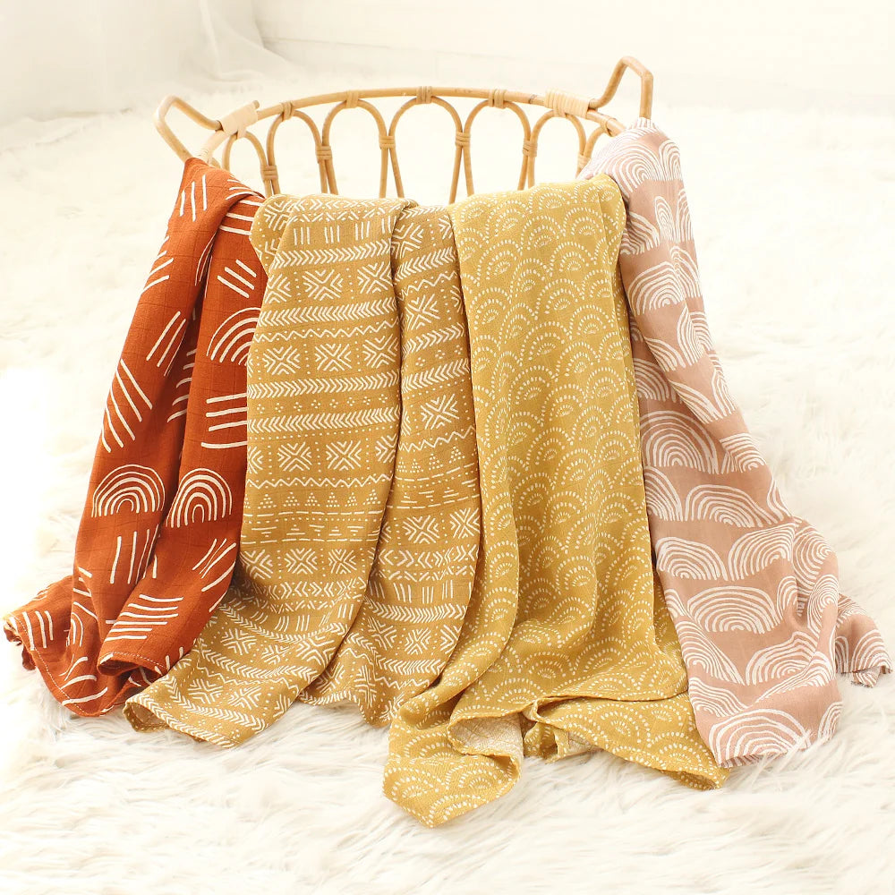 Une sélection de plaids Lange Bébé en Bambou & Coton aux tons terreux drapés avec désinvolture sur un panier tressé, apportant une touche cosy et bohème à la décoration intérieure, parfaite pour le confort de l'enfant par BABY PREMA.