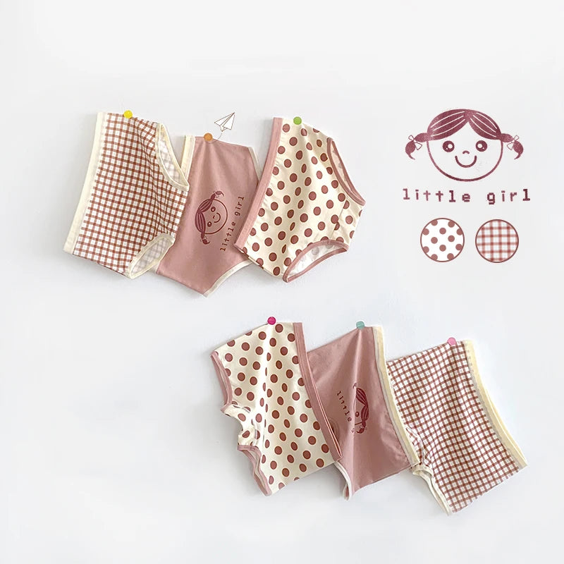 Un ensemble de sous-vêtements pour enfants, comprenant des imprimés à carreaux, à pois et dessins animés, disposés sur un fond blanc. Le texte « petite fille » et un simple visage de dessin animé se trouvent à côté des vêtements. Ce Lot de 3 Culottes pour Enfants de BABY PREMA est confectionné en coton doux doux pour un confort ultime.