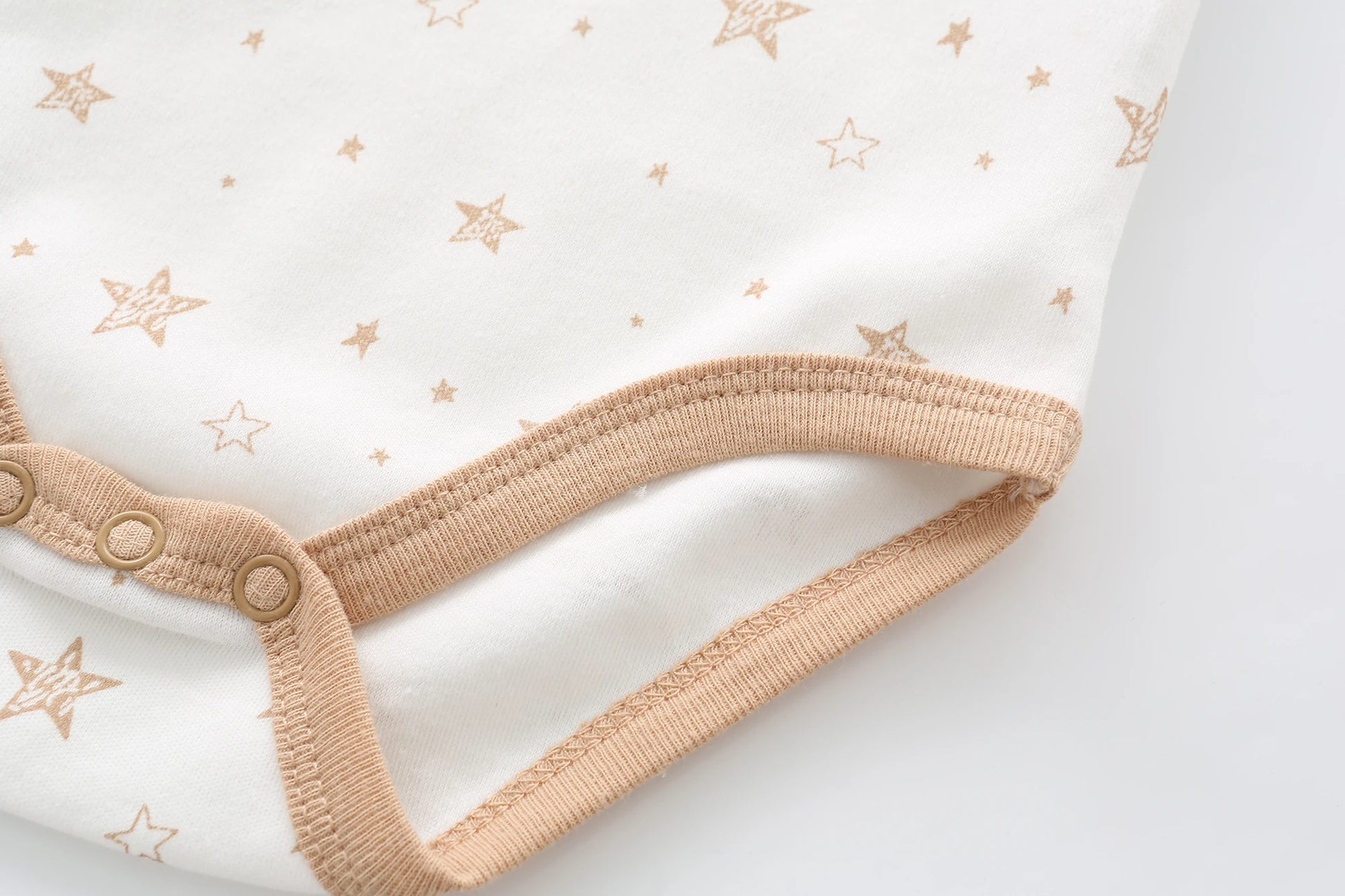 Gros plan d'une combinaison bébé d'un Lot de 5 Bodys Bébé | Coton Agréables & conforts de BABY PREMA, caractérisé par un motif étoilé beige avec une bordure marron clair et des boutons-pression le long du bas.