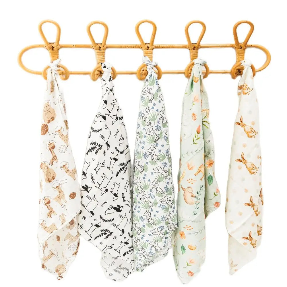 Un lot de cinq torchons de cuisine à motifs BABY PREMA dans des teintes douces, chacun présentant un motif différent, soigneusement accrochés à une tige de bambou avec des crochets métalliques sur un fond blanc.