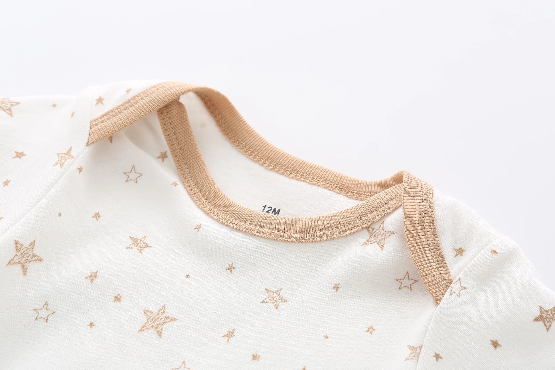 Une combinaison blanche pour bébé étiquetée « 12M » présente des motifs d'étoiles marron clair et une bordure beige autour de l'encolure. Cette adorable pièce, parfaite pour un trousseau de naissance, est confectionnée dans un coton doux et respirant pour assurer le confort de votre bébé. Il fait partie du Lot de 5 Bodys Bébé | Collection Coton Agréables & conforts par BABY PREMA.