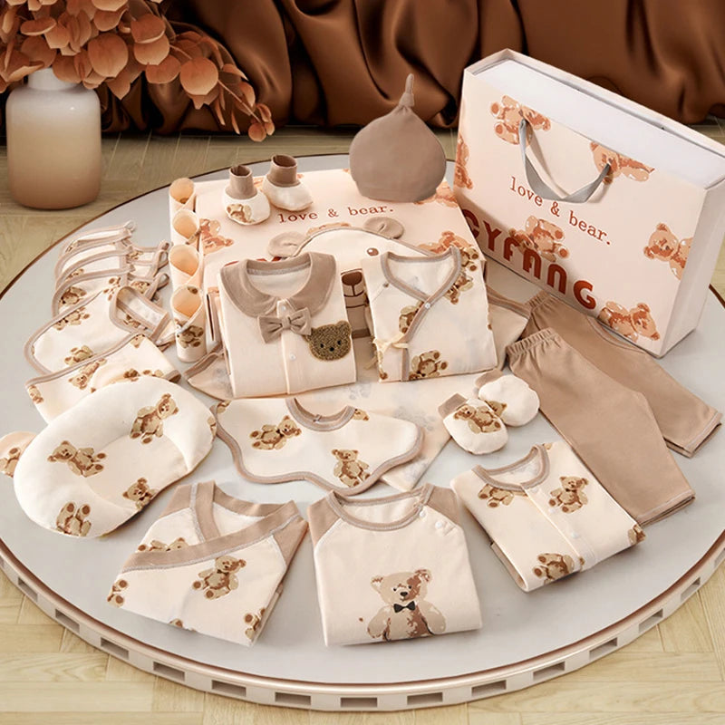 Une collection de vêtements et d'accessoires pour bébé aux motifs d'ours est exposée sur une table ronde. Ce Coffret Naissance Coton | Nouveau-nés Douceur Assurée de BABY PREMA comprend des vêtements, des bavoirs, des chapeaux, des mitaines, des chaussettes et un sac cadeau en coton doux et respirant.