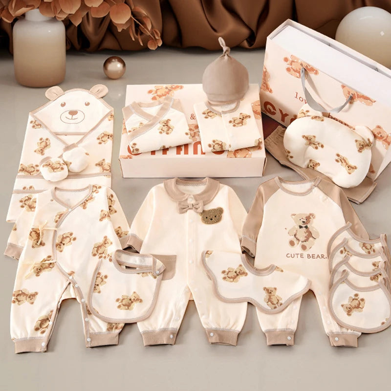 Un ensemble de vêtements pour bébé est présenté, comprenant des grenouillères, des bavoirs, un bonnet, une couverture, un oreiller et des moufles, le tout avec des motifs d'ours en peluche dans des couleurs neutres. Ce *Coffret Naissance Coton* de BABY PREMA assure le confort avec du *coton doux et respirant*. À proximité se trouvent des bougies décoratives et un coffret cadeau.