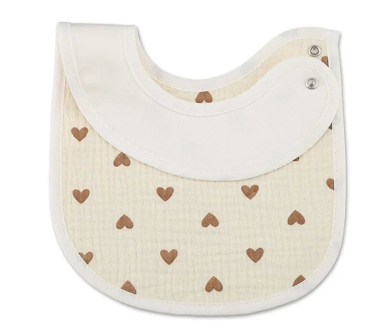 Un bavoir bébé beige avec une bordure blanche et des motifs cœurs marron. Le modèle BABY-PREMA Bavoirs Motifs Bébé 2 Pièces comporte deux boutons-pression dans le coin supérieur droit pour la fermeture.
