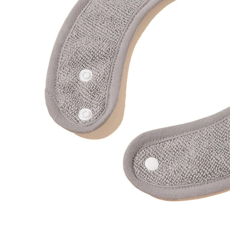Gros plan de deux pans d'un article en tissu gris texturé avec des bords arrondis et un bouton pression blanc, ressemblant aux Bavoirs Bébé Lot de 4 Pièces de BABY-PREMA. Le tissu semble doux avec une surface bouclée comme du tissu éponge. Disposé dans une forme incurvée, presque semi-circulaire, sur un fond blanc uni.