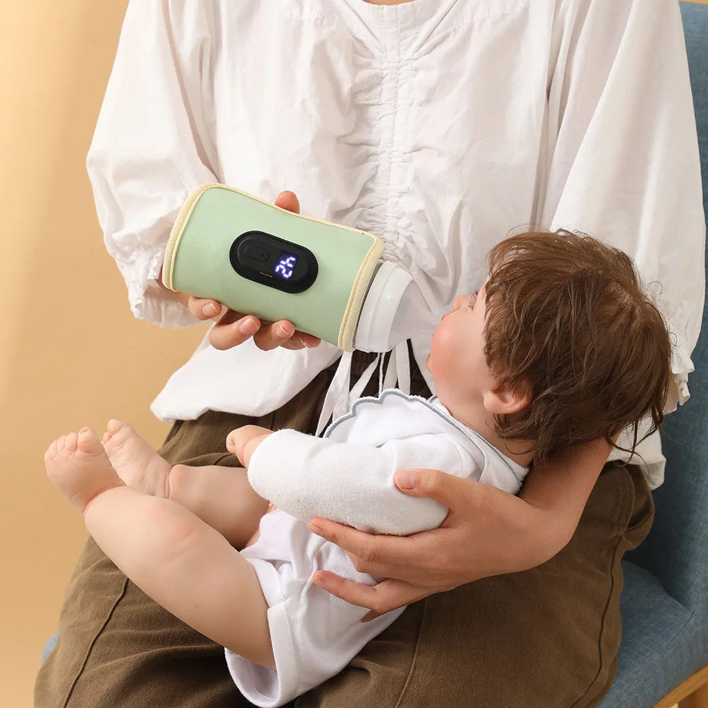 Une personne en chemise blanche donne le biberon à un bébé vêtu de blanc, assis sur ses genoux. Le Chauffe-Biberon Portable multifonction de BABY-PREMA, équipé d'un affichage numérique, indique "25°C". Le fond est d’une simple couleur beige.