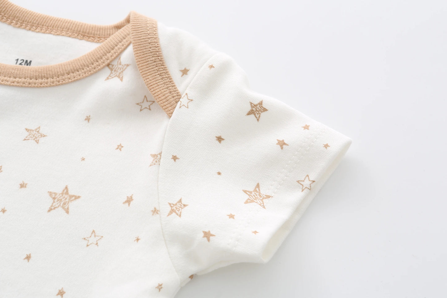 Gros plan sur un Lot de 5 Bodys Coton blanc | Agréables & Conforts de BABY PREMA aux motifs étoiles marron clair. Le vêtement présente des manches courtes, une bordure marron à l'encolure et des boutons-pression pour plus de commodité. L'étiquette de taille indique "12M", assurant un confort optimal pour votre tout-petit.