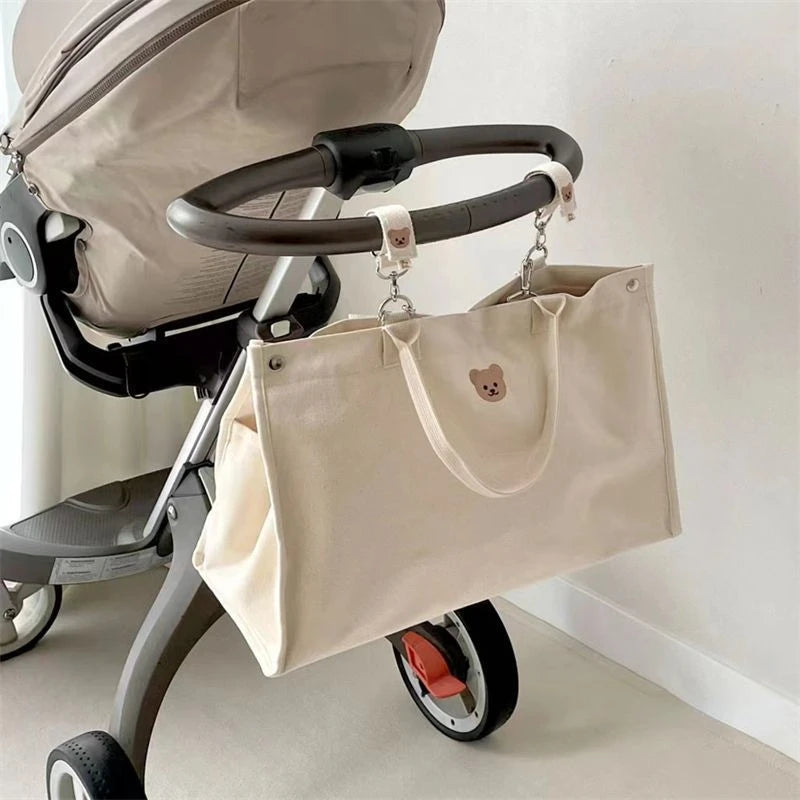 Sac à Langer Bébé Fourre Tout Beige avec un joli bouton suspendu au guidon d'une poussette moderne et élégante, prêt pour une journée avec les essentiels de bébé en remorque, parfait pour tous les parents de BABY-PREMA.