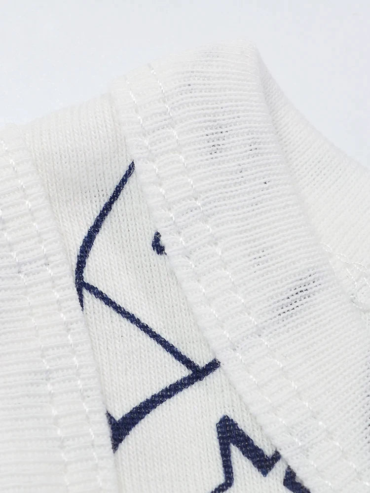 Image en gros plan d'un tissu blanc avec coutures apparentes et vue partielle d'un graphisme bleu marine, éventuellement du BABY PREMA Pack Cadeau 3 Bodies Bébé d'été. La texture du tissu est apparente, mettant en valeur les détails de la maille et la précision de la couture.