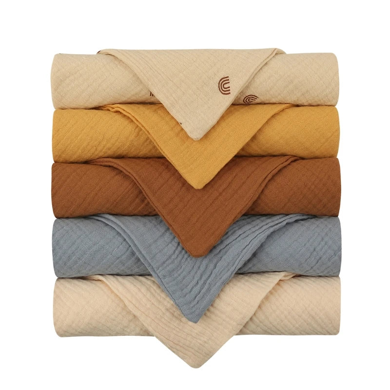 Un assortiment soigneusement empilé de couettes ou couvertures pliées Lot de 5 Langes Bébé en Coton dans une palette de couleurs harmonieuse allant du crème à la moutarde, en passant par la rouille et les nuances froides de bleu, chacune choisie pour son poids léger idéal pour enf BABY PREMA.