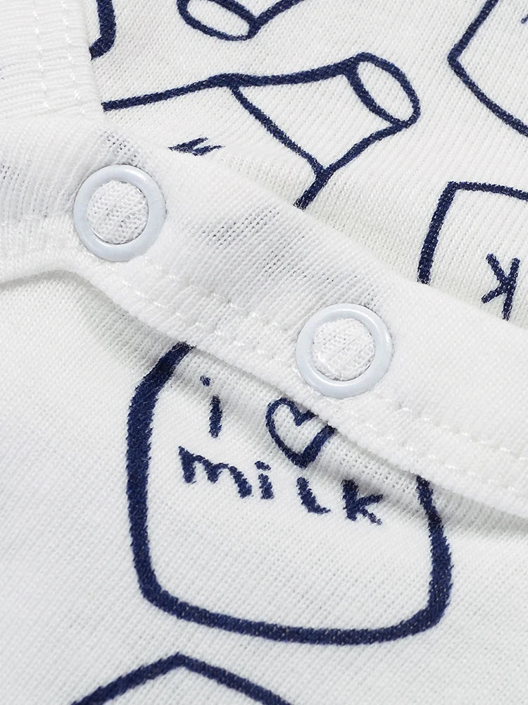 Gros plan sur un Pack Cadeau 3 Bodies Bébé d'été blanc avec un devant boutonné et des illustrations imprimées en bleu. Les dessins comprennent des cartons de lait, des bouteilles et un pot avec « i ♥ milk » écrit à l'intérieur. Cette charmante pièce de BABY PREMA présente des boutons blancs attachés à une bande de tissu avec surpiqûres.