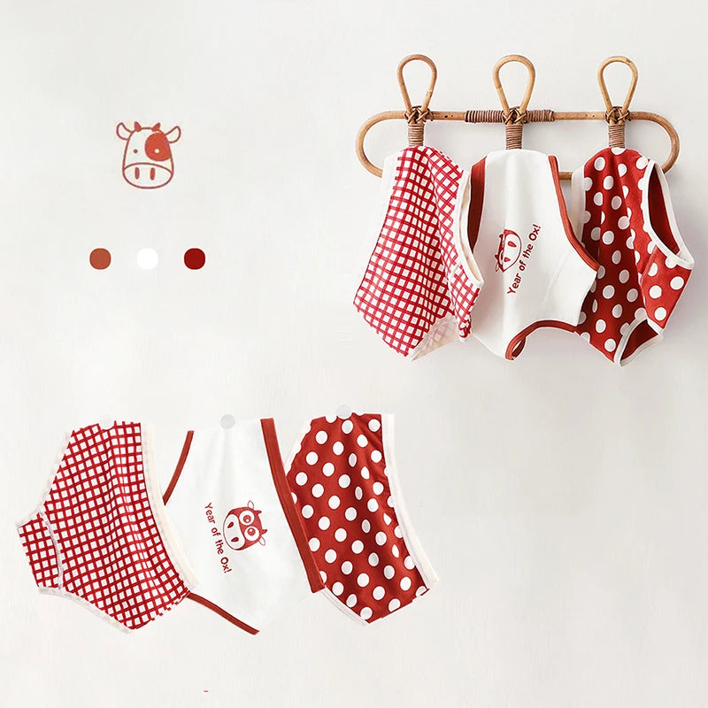 Cinq caleçons pour enfants aux motifs rouges et blancs (à carreaux et à pois) sont suspendus sur un cintre en bambou sur fond blanc. Doté d'une matière en coton doux, ce Lot de 3 Culottes pour Enfants de BABY PREMA est orné de charmantes illustrations de vaches affichées à côté d'elles.