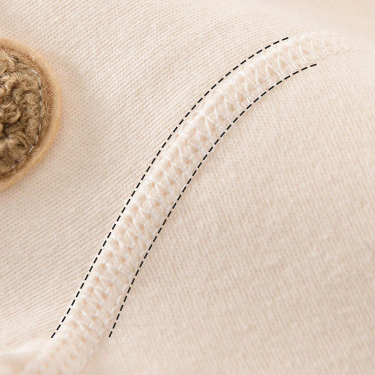 Vue rapprochée d'un tissu beige avec des coutures détaillées et un bouton tricoté, confectionné en coton doux et respirant. Le Coffret Naissance Coton | Nouveau-nés Douceur Assurée de BABY PREMA comprend 20 à 26 pièces essentielles pour le confort de votre bébé.