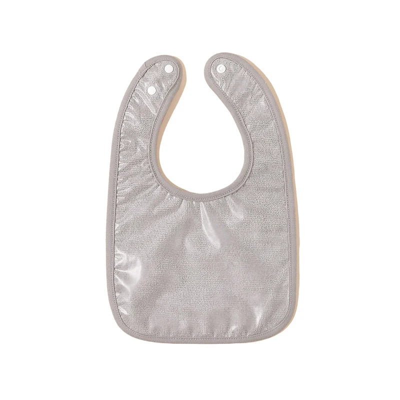 Un bavoir gris pour bébé avec un devant lisse et résistant à l'eau et deux boutons-pression renforcés au niveau du cou pour une fermeture réglable. Ce BABY-PREMA Bavoirs Bébé Lot de 4 Pièces présente un design simple mais fonctionnel, idéal pour garder les vêtements propres pendant l'allaitement.