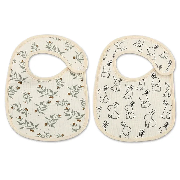 Deux bavoirs pour bébé avec fermetures à pression, l'un avec un motif de feuilles vertes et l'autre avec un motif de lapin noir et blanc. Ces Bavoirs Motifs Bébé 2 Pièces de BABY-PREMA offrent à la fois style et praticité pour tout désordre à l'heure des repas.