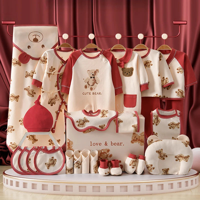 Le Coffret Naissance Coton | Nouveau-nés Douceur Assurée de BABY PREMA est un ravissant ensemble de vêtements et d'accessoires pour bébé aux motifs d'oursons rouges et beiges. Fabriqué en coton doux et respirant, cet ensemble comprend des grenouillères, des bavoirs, des bonnets, des mitaines, des serviettes et des couvertures. Il est élégamment présenté sur un support avec un rideau rouge en toile de fond.
