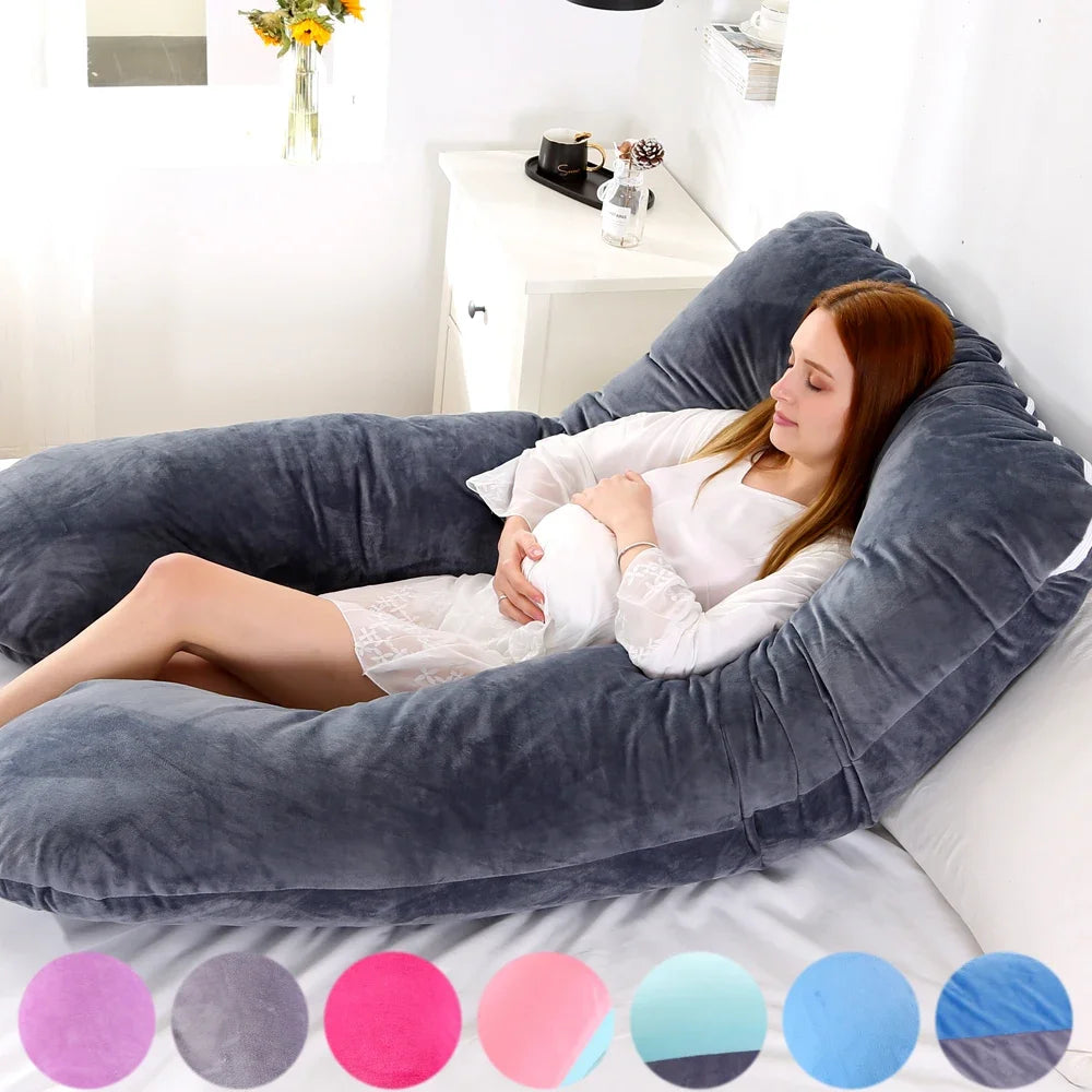 Une femme s'allonge dans un grand Coussin de Maternité & Allaitement BABY PREMA gris sur un lit dans une pièce doucement éclairée, bénéficiant de soutien et de confort. Vêtue d'une tenue blanche, elle apparaît détendue. Devant l'image se trouvent huit petits cercles affichant différentes couleurs d'oreillers similaires, idéaux pour toute femme enceinte.