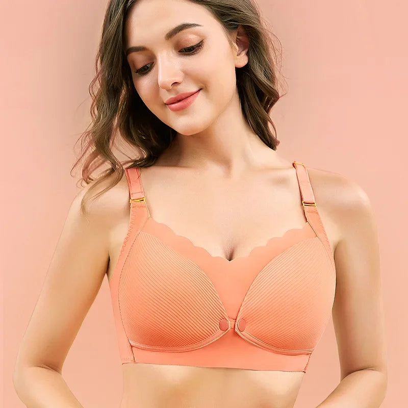 Une petite femme présentant un soutien-gorge BABY PREMA Soutien de Grossesse & Allaitement couleur pêche avec bordure festonnée sur fond rose tendre.
