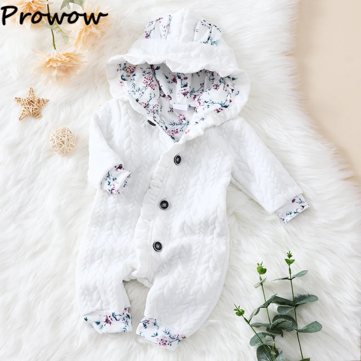 Une combinaison bébé blanche et confortable avec une capuche est exposée sur une surface douce et poilue. La Combinaison pour Nouveau-nés BABY PREMA présente un motif texturé et une doublure à imprimé floral sur la capuche et les poignets. Il est orné de trois boutons noirs et entouré d'une petite étoile décorative, d'une fleur et de verdure.