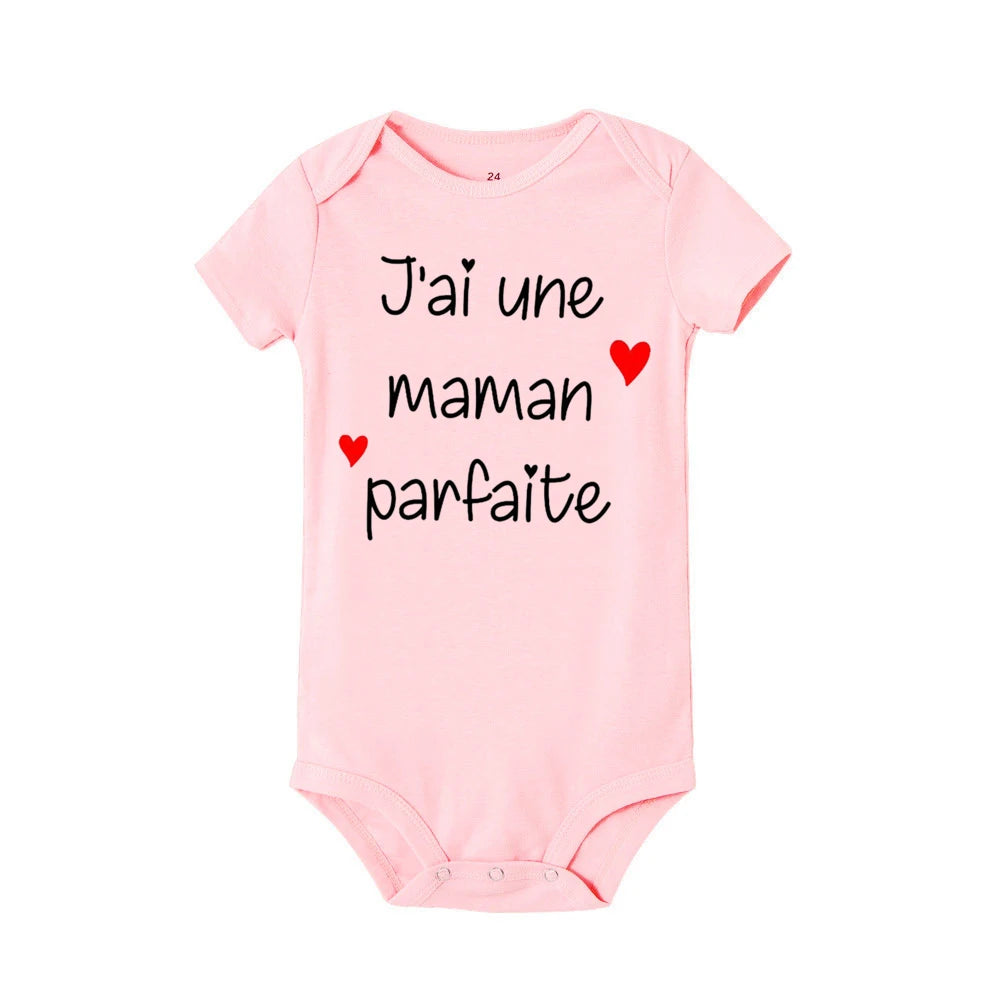 Un Body Bébé Coton Imprimé Préma rose avec des manches courtes comportant la phrase française "J'ai une maman parfaite" en texte noir, accompagnée de deux petits coeurs rouges. Cet adorable bébé BABY-PREMA est un ajout charmant à toute barboteuse-robe enfant.