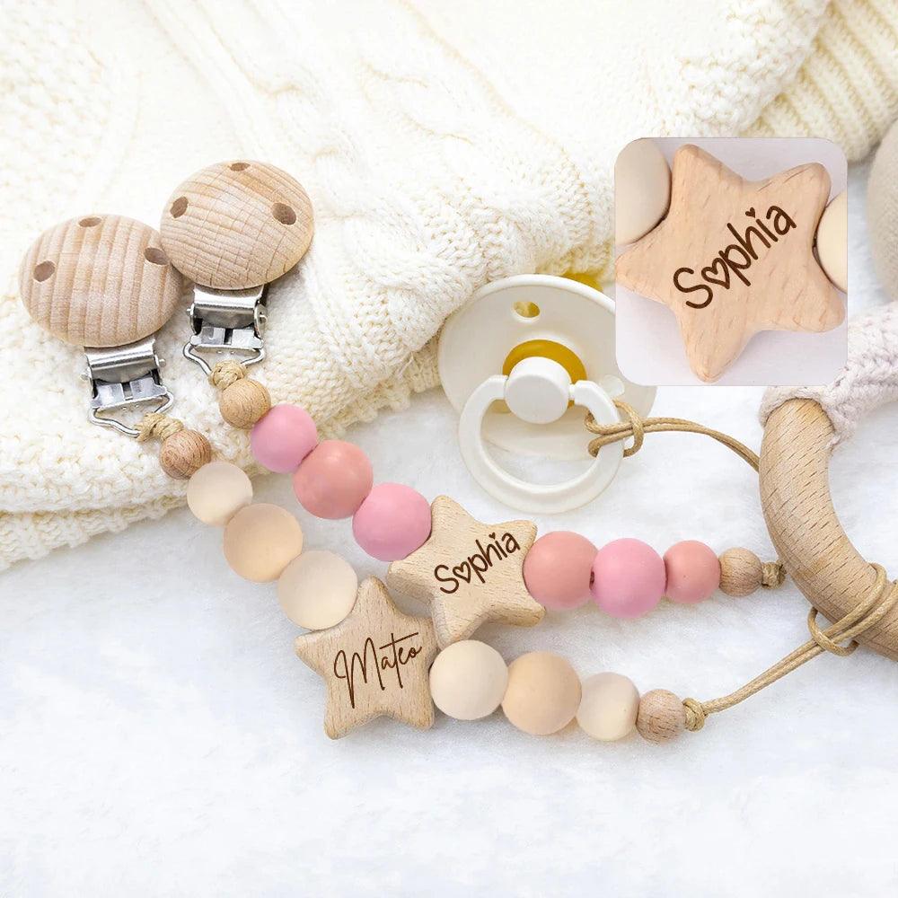 Accessoires bébé personnalisés comprenant une attache-sucette Attache Sucette Bébé Personnalisé, des perles de dentition et une étiquette nominative personnalisée en forme d'étoile, disposés sur une douce couverture blanche. (Nom de marque : BÉBÉ-PREMA)
