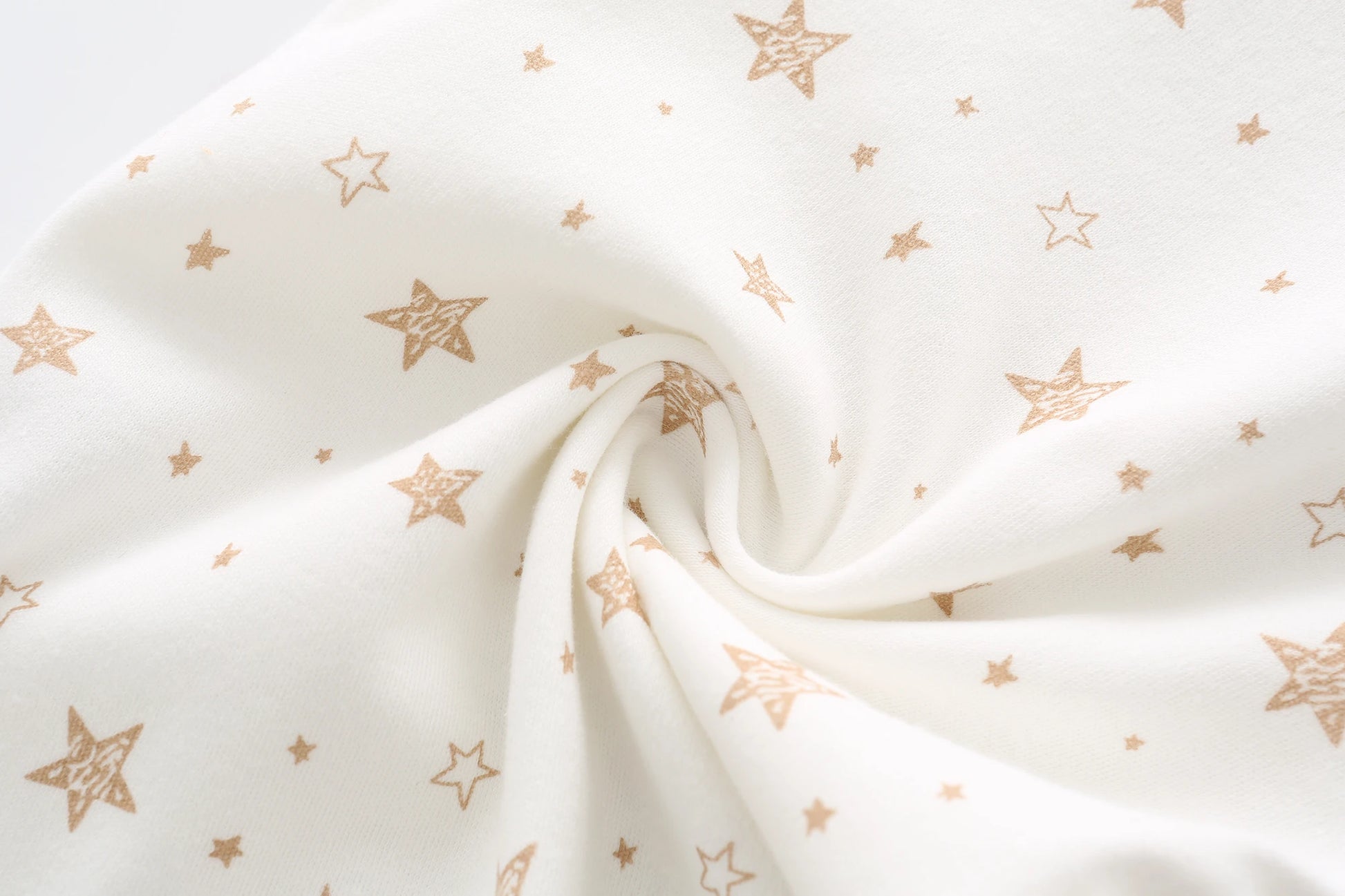 Image en gros plan d'un tissu blanc avec de petits motifs d'étoiles dispersés en marron clair. Le tissu est légèrement torsadé au centre, ressemblant à la texture douce et au confort de BABY PREMA Lot de 5 Bodys Coton | Agréables & Conforts.