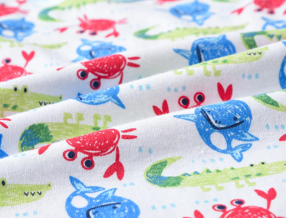 Image en gros plan d'un tissu avec des illustrations d'animaux ludiques, semblables à celles d'un dessin animé. Le motif présente des crabes rouges, des alligators verts et des baleines bleues, tous souriants et entourés de petits points colorés sur fond blanc. Parfait pour créer des barboteuses sans manches, le coton doux et respirant est idéal pour un bébé BABY PREMA Lot de 3 Bodies.