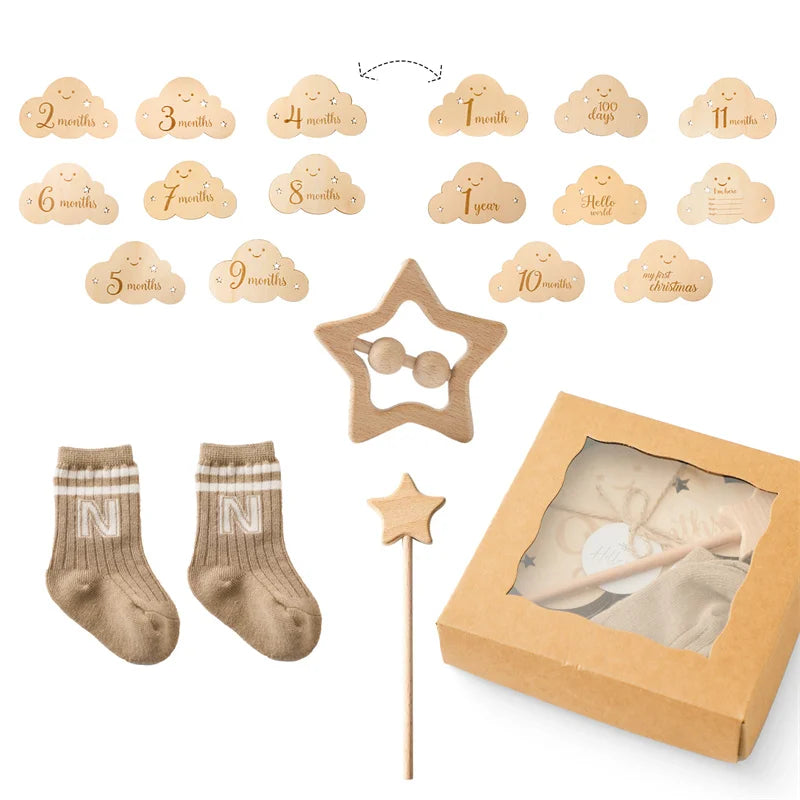 Un coffret BABY PREMA Coffret Cadeau Naissance Bébé composé de nuages en bois marquant les âges de un à douze mois, une paire de chaussettes avec la lettre « n » dessus, un cadre photo étoile en bois, une baguette article bébé en forme d'étoile.